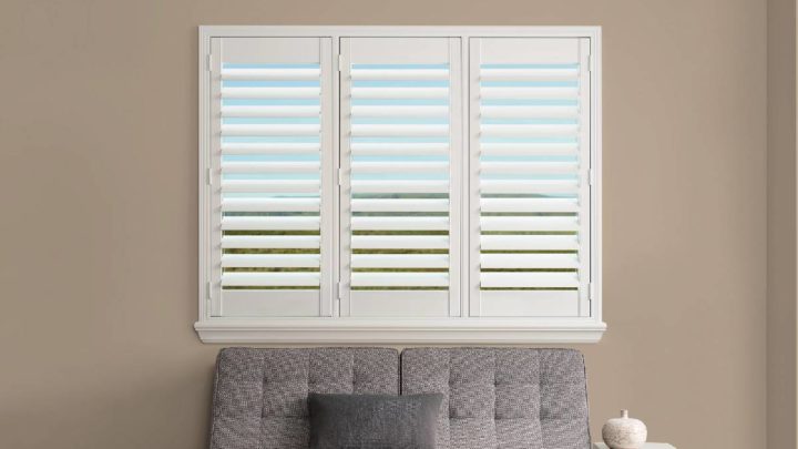 Small gray couch sitting beneath a window covered with Hunter Douglas Palm Beach™ PolySatin™ Shutters at White House Designs for Life near Fairfield, NJ